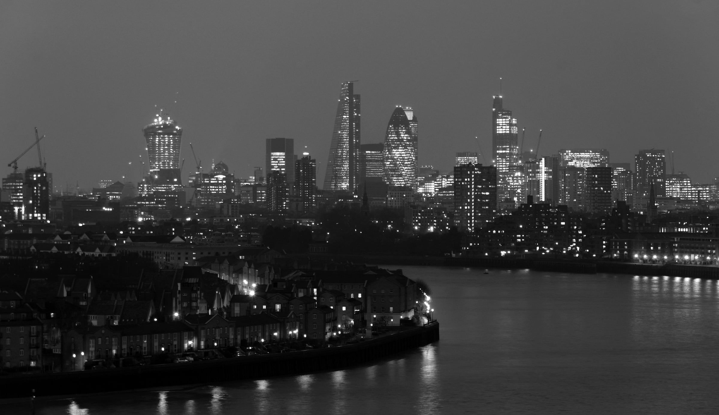 The River Thames curving towards the lit towers of the City of London at dusk.
